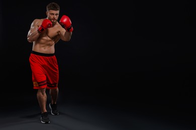 Man in boxing gloves fighting on black background. Space for text