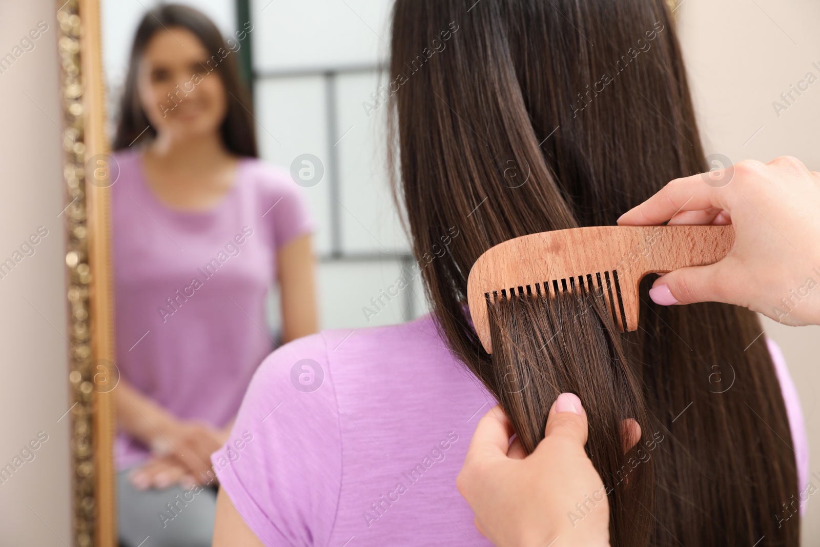 Photo of Woman combing friend's hair indoors, closeup view