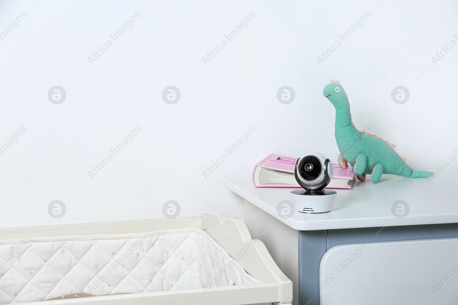 Photo of Baby camera with toy and photo album on chest of drawers near crib in room, space for text. Video nanny