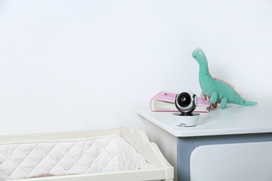Photo of Baby camera with toy and photo album on chest of drawers near crib in room, space for text. Video nanny