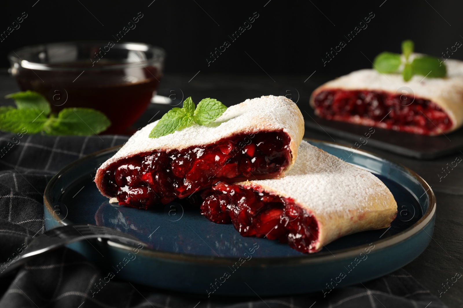 Photo of Delicious strudel with cherries, powdered sugar and mint on table, closeup