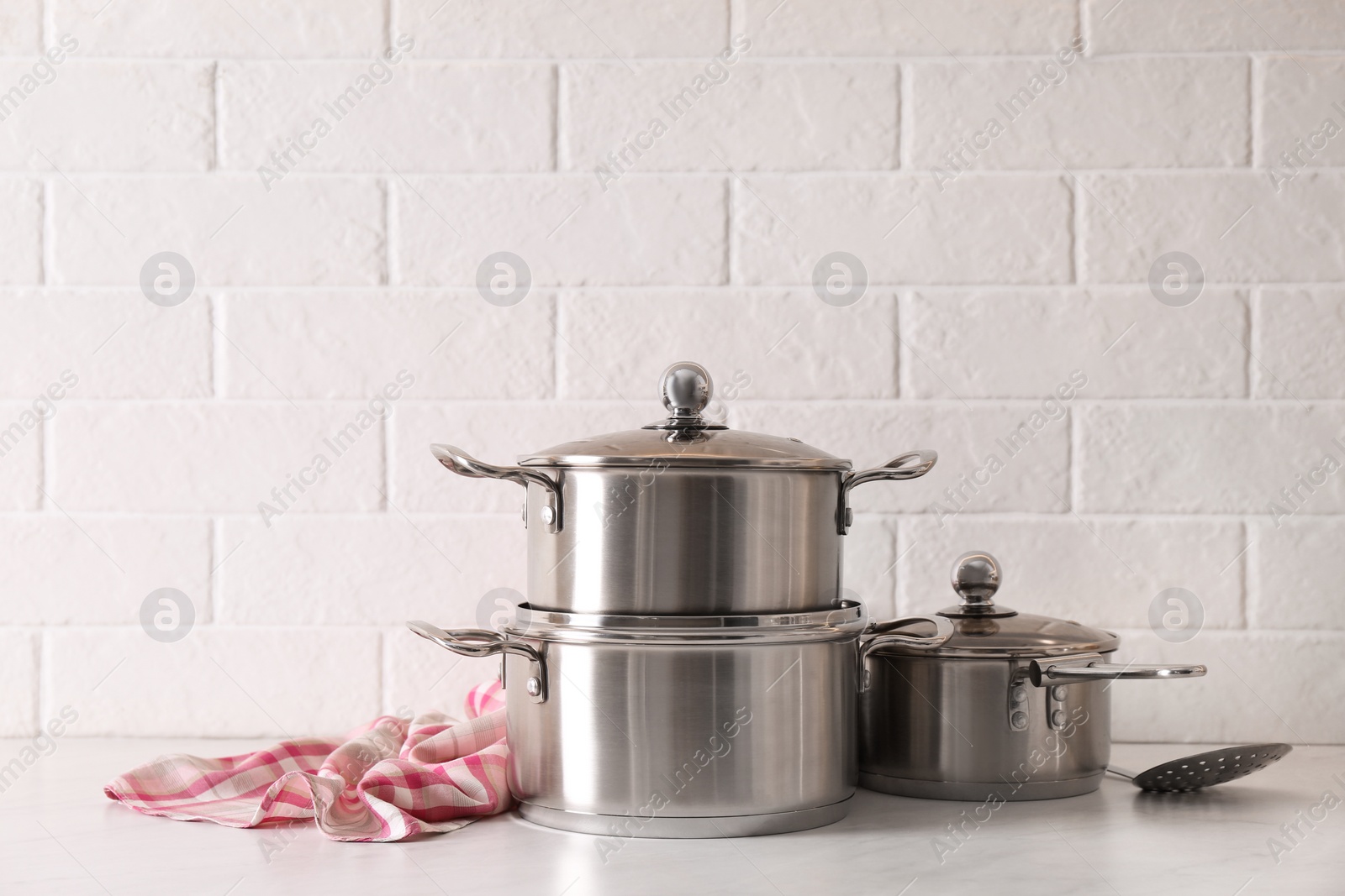 Photo of Set of stainless steel cookware on table near white brick wall