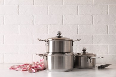 Photo of Set of stainless steel cookware on table near white brick wall