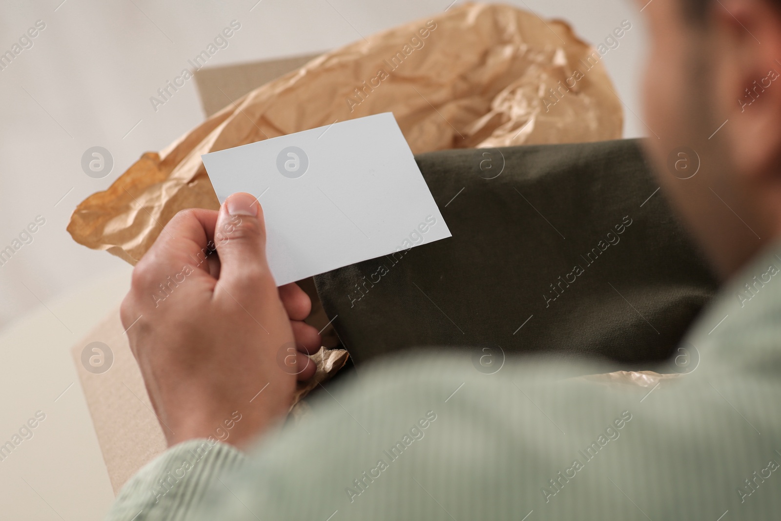 Photo of Young man holding greeting card near parcel with Christmas gift, closeup