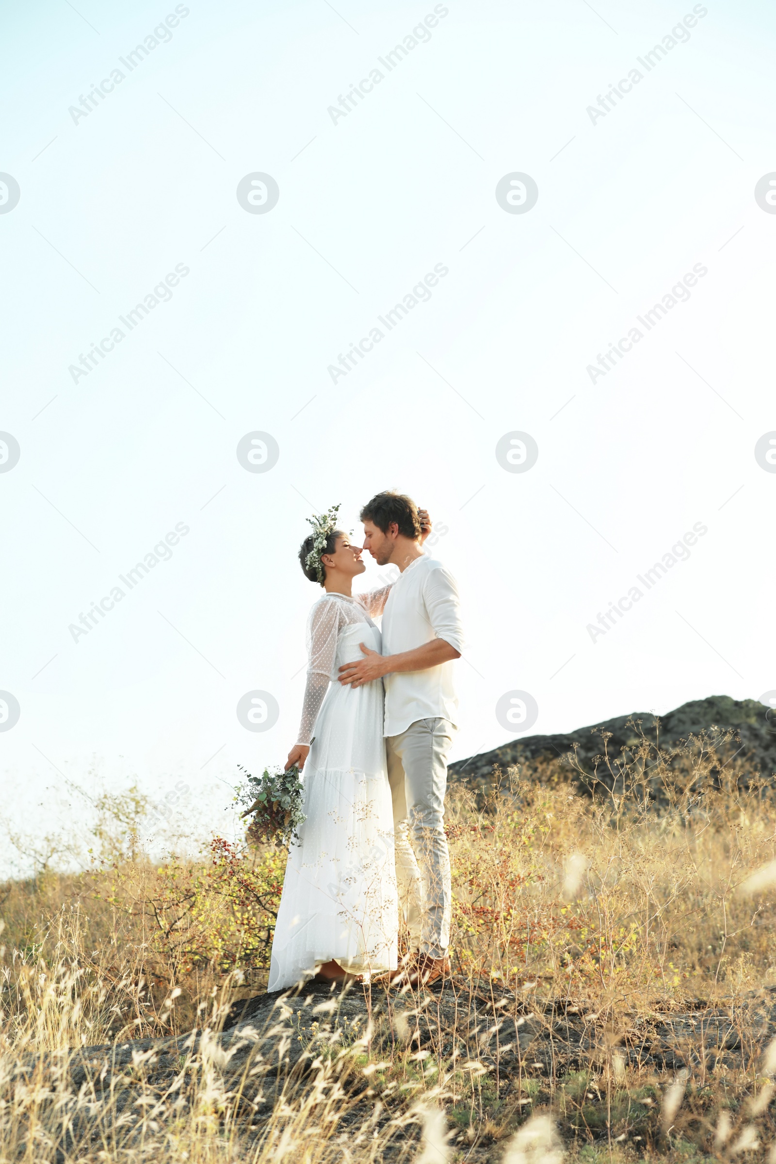 Photo of Happy newlyweds with beautiful field bouquet outdoors