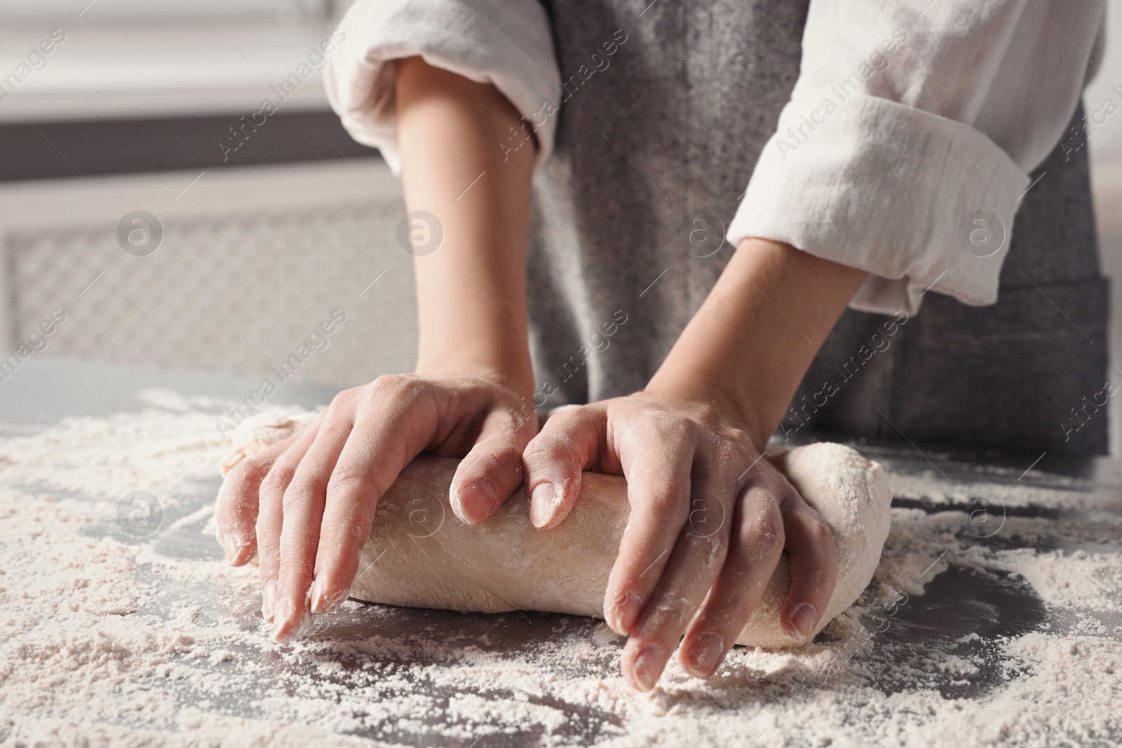 Photo of Woman kneading dough at table in kitchen, closeup