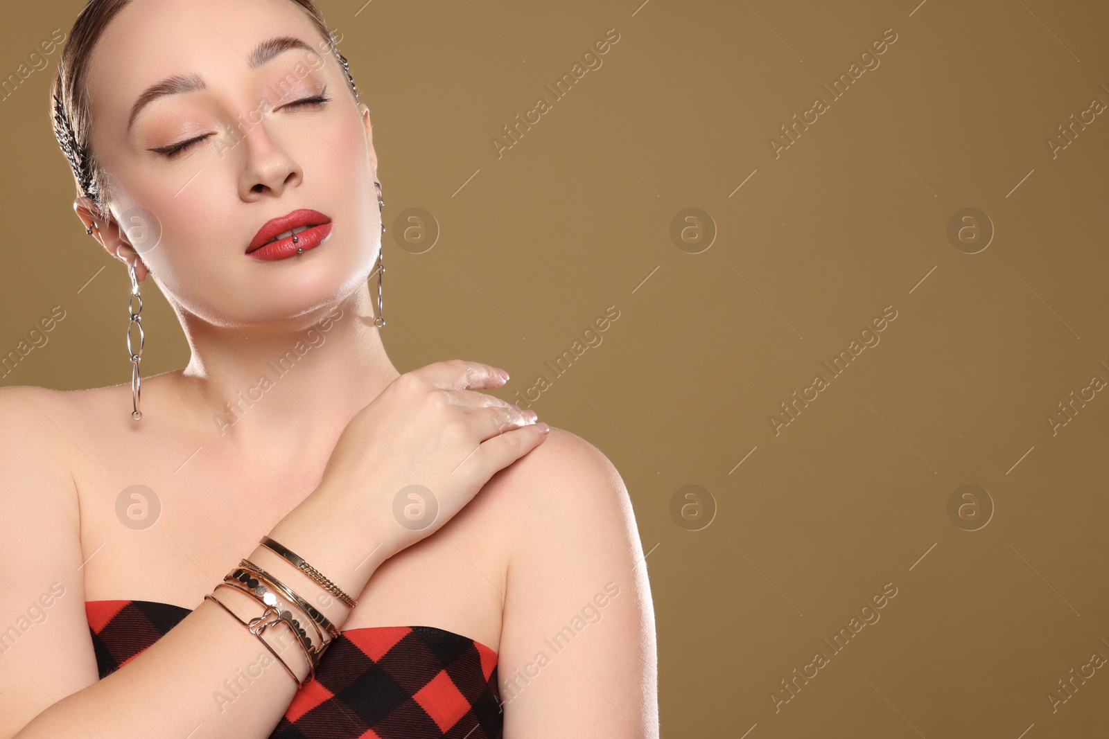 Photo of Young woman with lip and ear piercings on light brown background, space for text