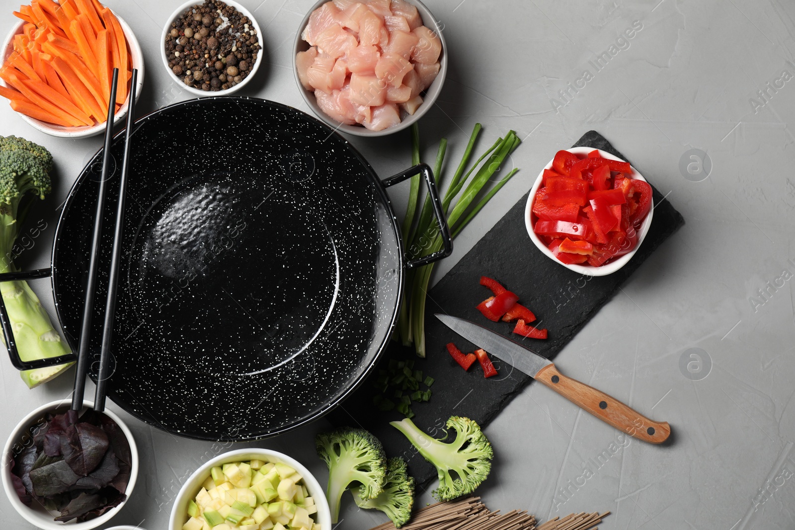 Photo of Wok pan, chicken and other products on light grey table, flat lay