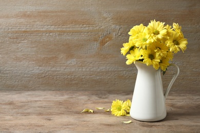 Photo of Jug with beautiful chamomile flowers on wooden table. Space for text