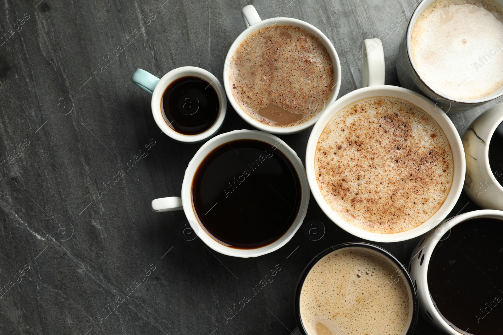 Photo of Many cups of different coffees on slate table, flat lay. Space for text