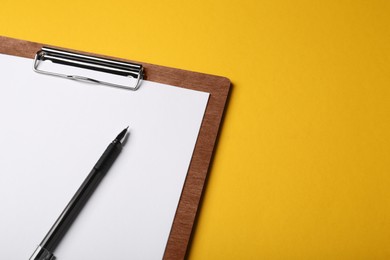 Wooden clipboard with sheet of blank paper and pen on yellow background. Space for text