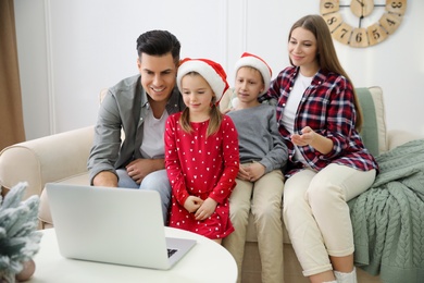 Family with children using video chat on laptop in room decorated for Christmas