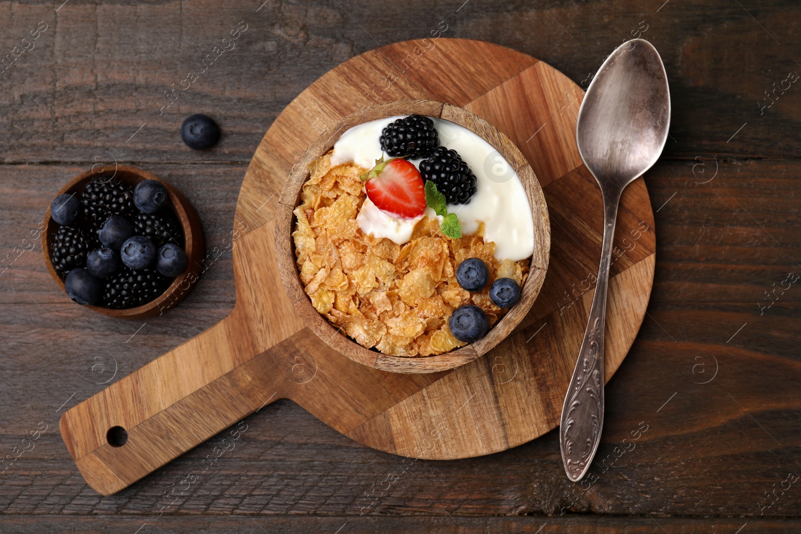 Photo of Delicious crispy cornflakes, yogurt and fresh berries served on wooden table, flat lay. Healthy breakfast