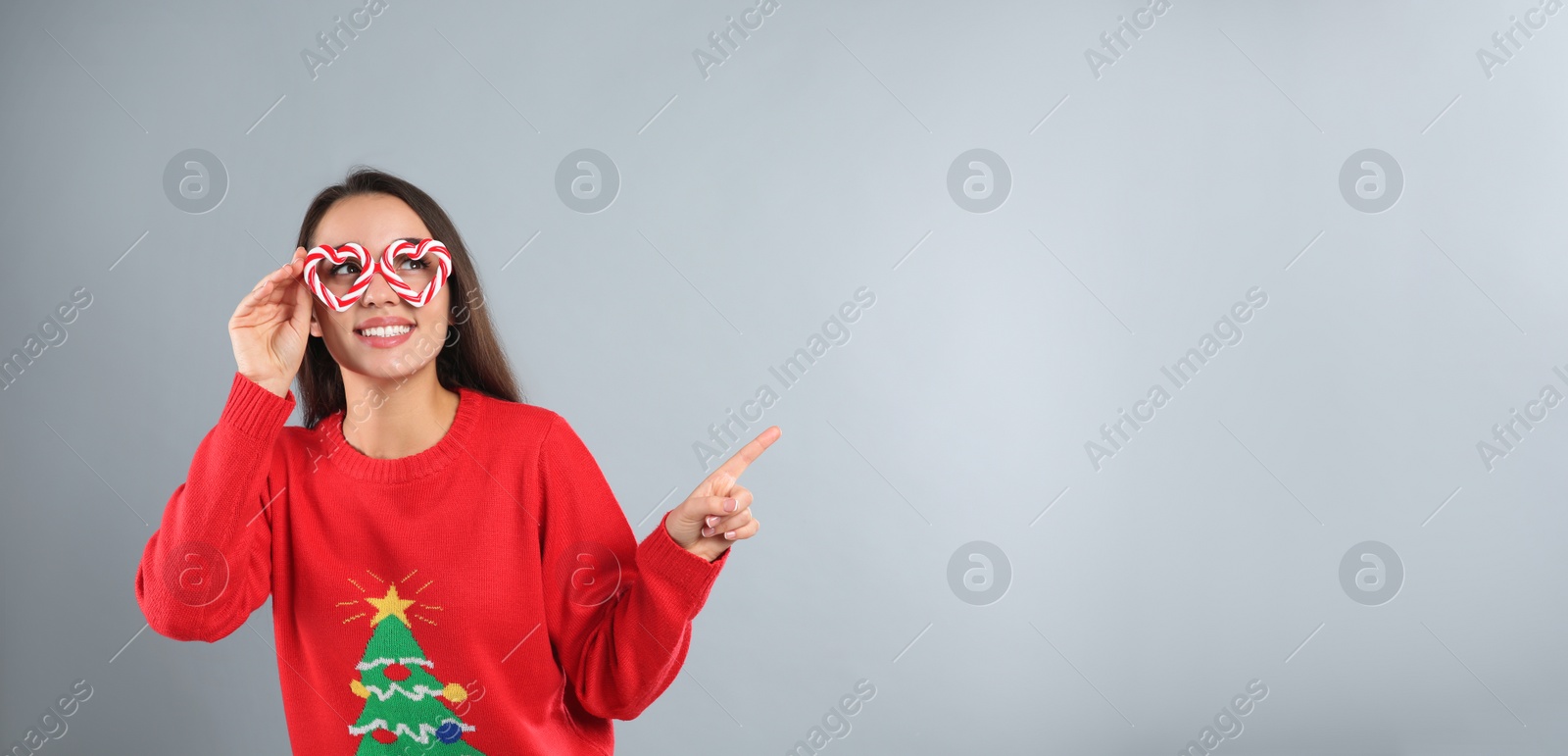 Photo of Young woman in Christmas sweater and party glasses on grey background, space for text