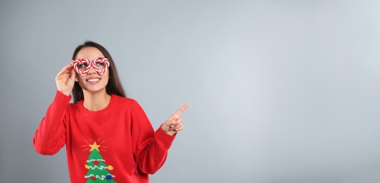 Young woman in Christmas sweater and party glasses on grey background, space for text