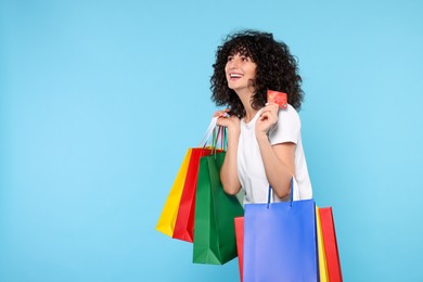 Happy young woman with shopping bags and credit cards on light blue background. Space for text