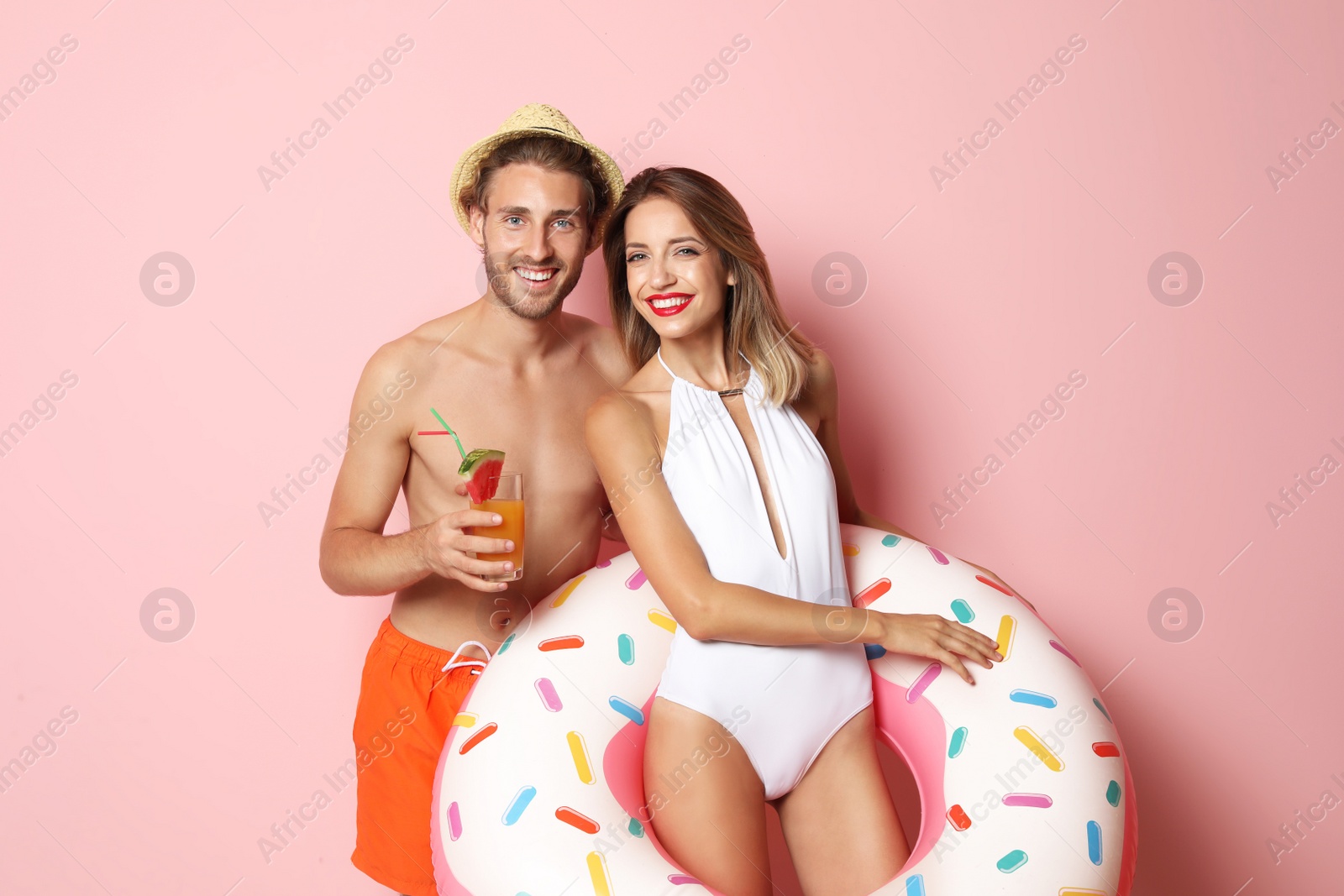 Photo of Happy young couple in beachwear with inflatable ring and cocktail on color background