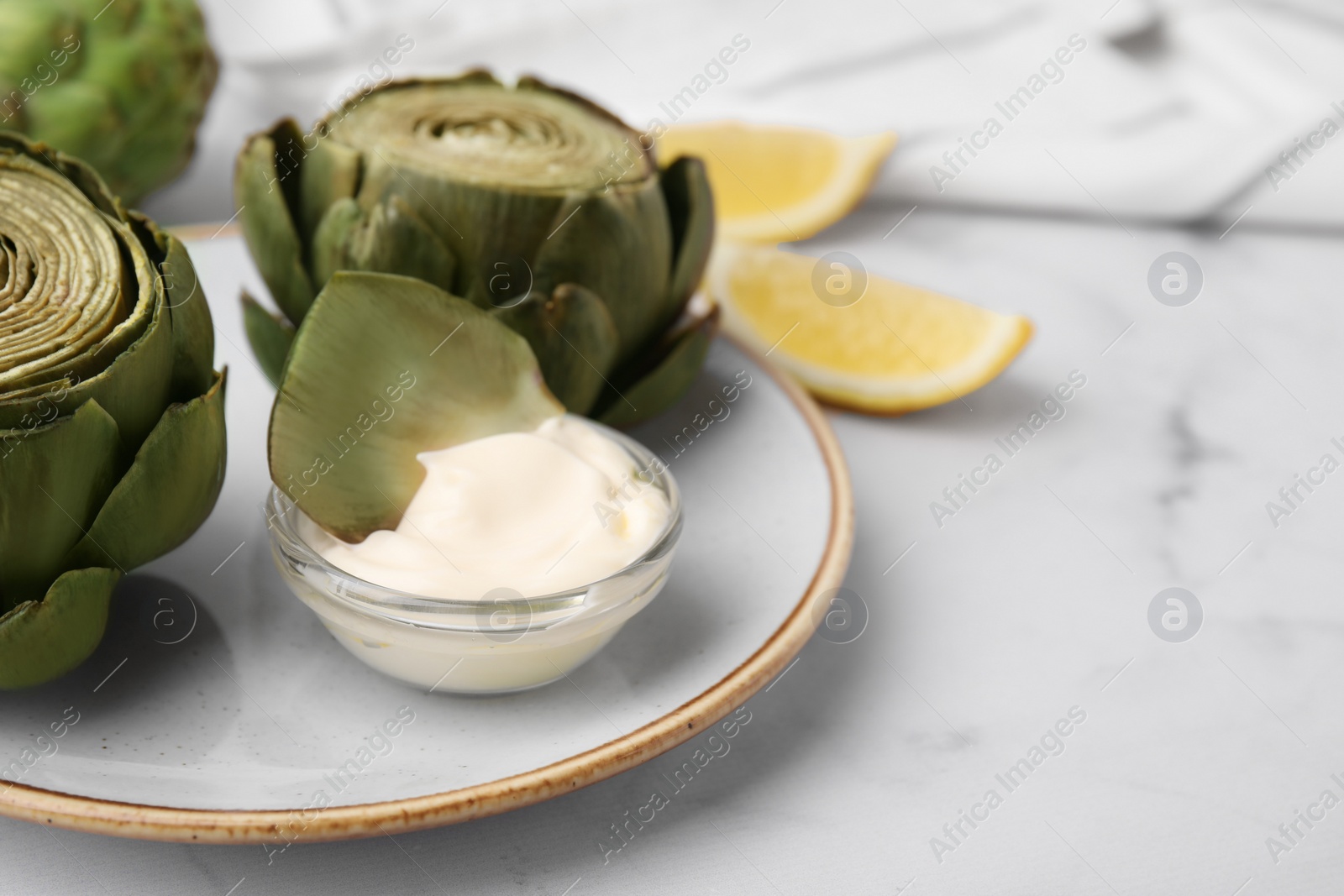 Photo of Delicious cooked artichokes with tasty sauce served on white marble table, closeup. Space for text