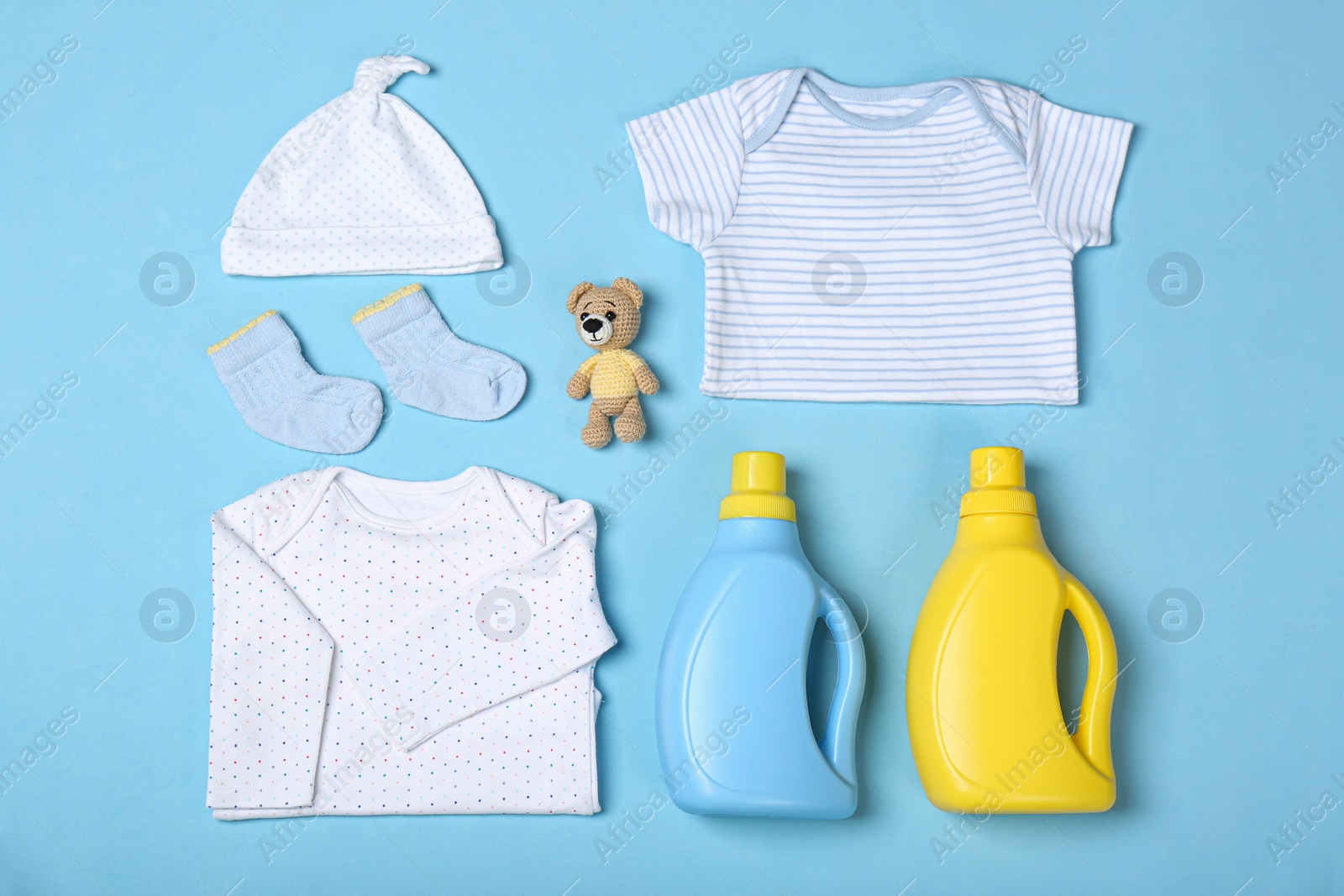 Photo of Flat lay composition with bottles of detergent and children's clothes on light blue background