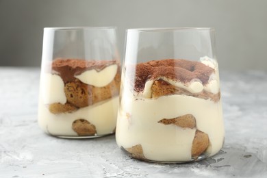 Photo of Delicious tiramisu in glasses on grey textured table, closeup