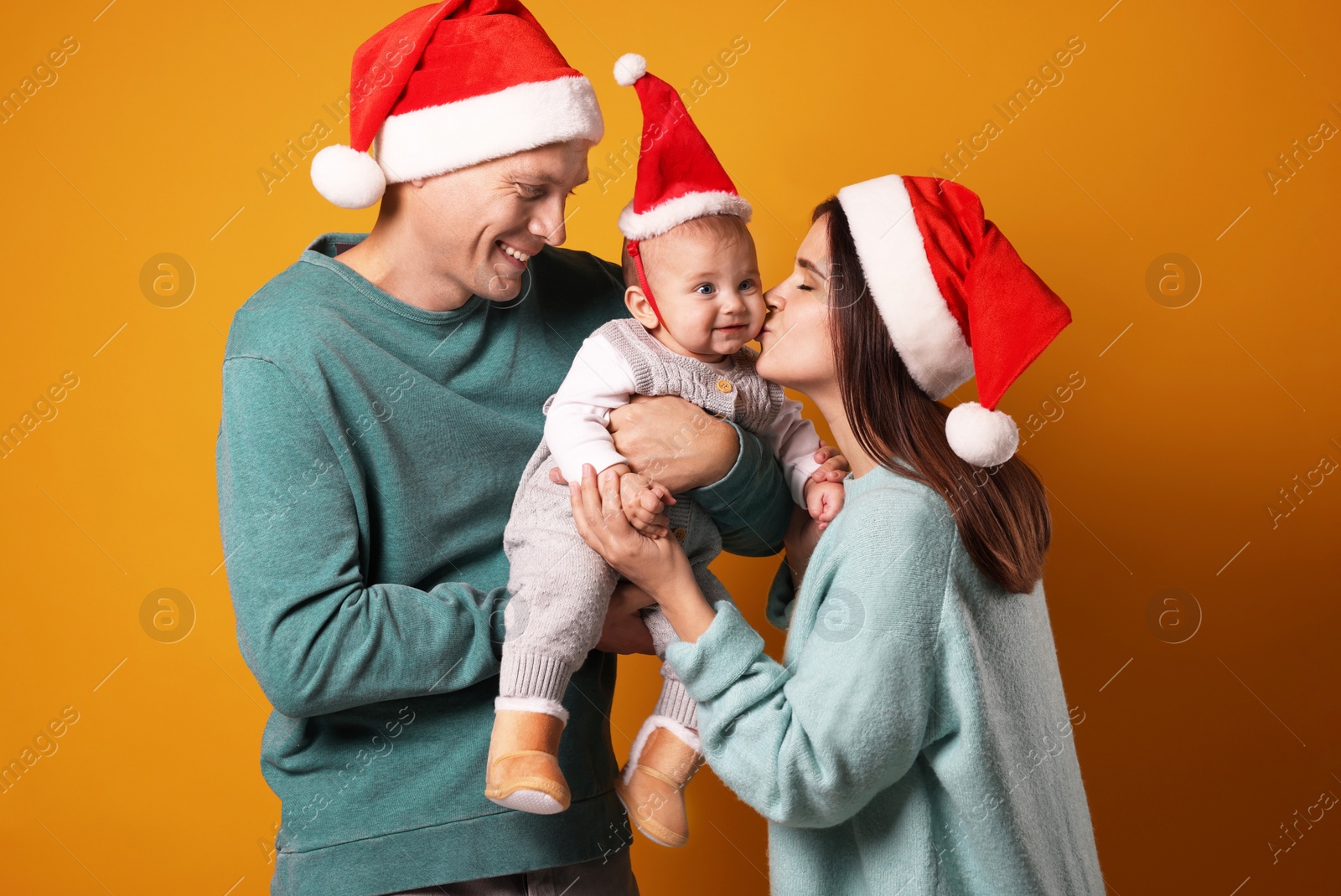 Photo of Happy couple with cute baby wearing Santa hats on yellow background. Christmas season