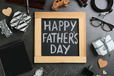 Photo of Chalkboard with phrase HAPPY FATHER'S DAY and male accessories on stone background, flat lay