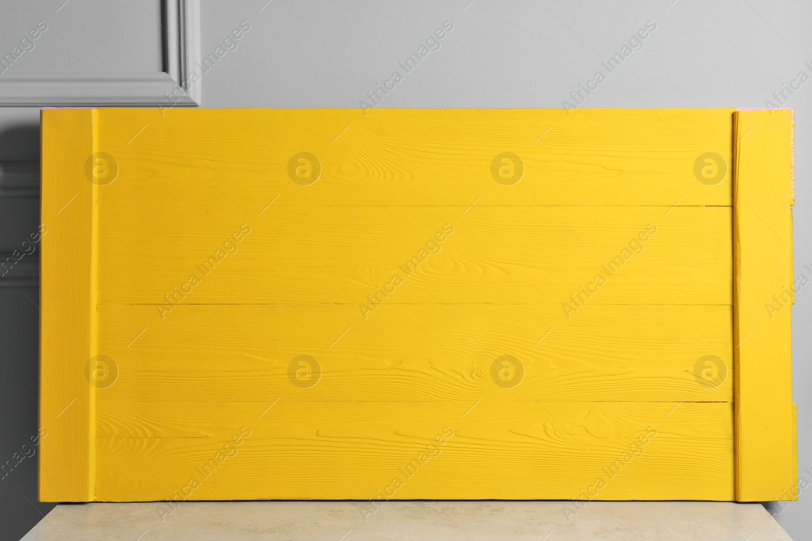 Photo of Yellow wooden board on table near light grey wall