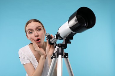 Surprised astronomer with telescope on light blue background