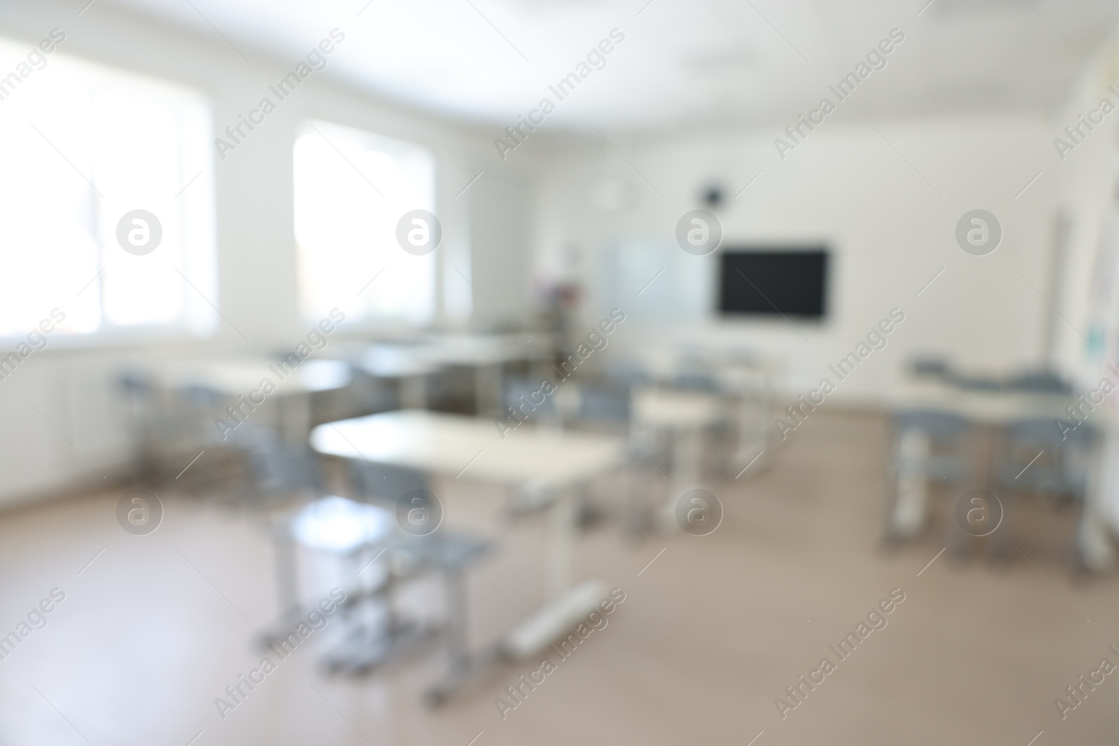 Photo of Blurred view of empty school classroom with desks, windows and chairs