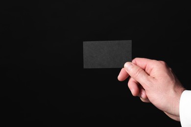 Businessman holding blank business card on black background, closeup. Space for text