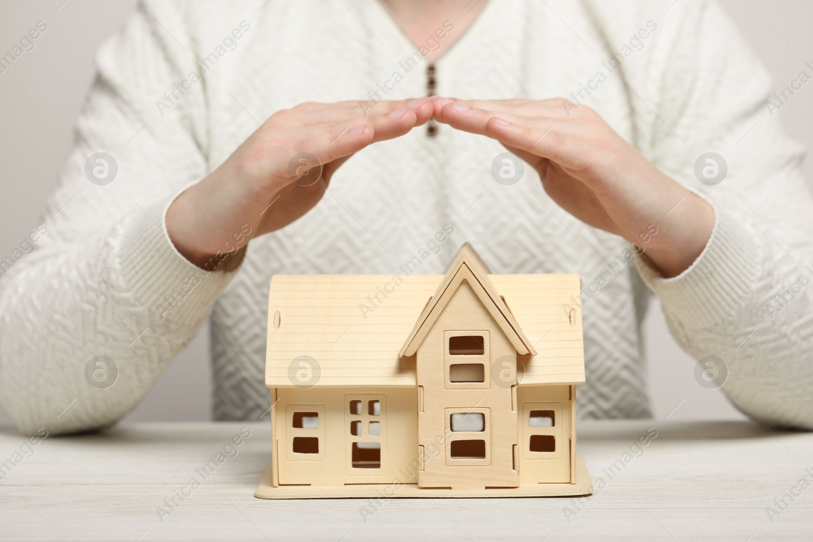 Photo of Home security concept. Man covering house model at white wooden table, closeup