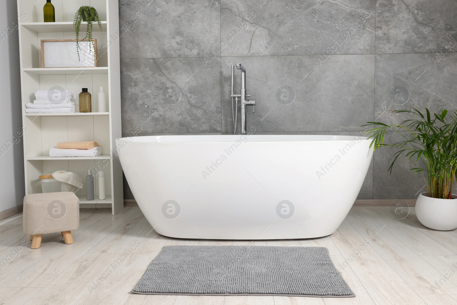 Photo of Stylish bathroom interior with ceramic tub, care products and towels in cabinet