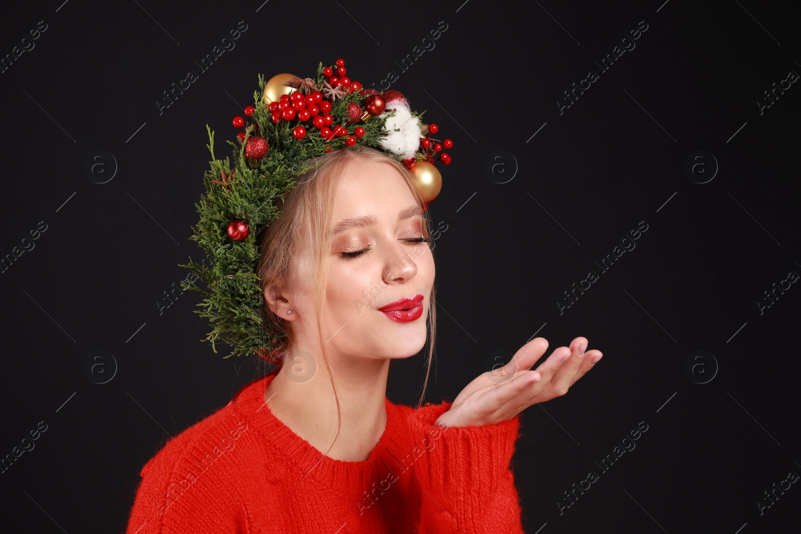 Photo of Beautiful young woman wearing Christmas wreath on black background