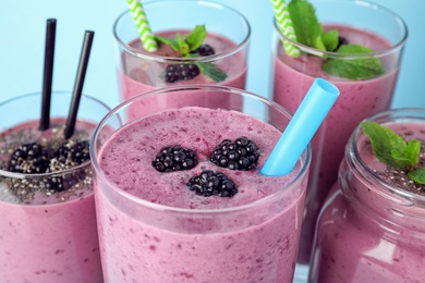 Delicious blackberry smoothie in different glassware on light blue background, closeup