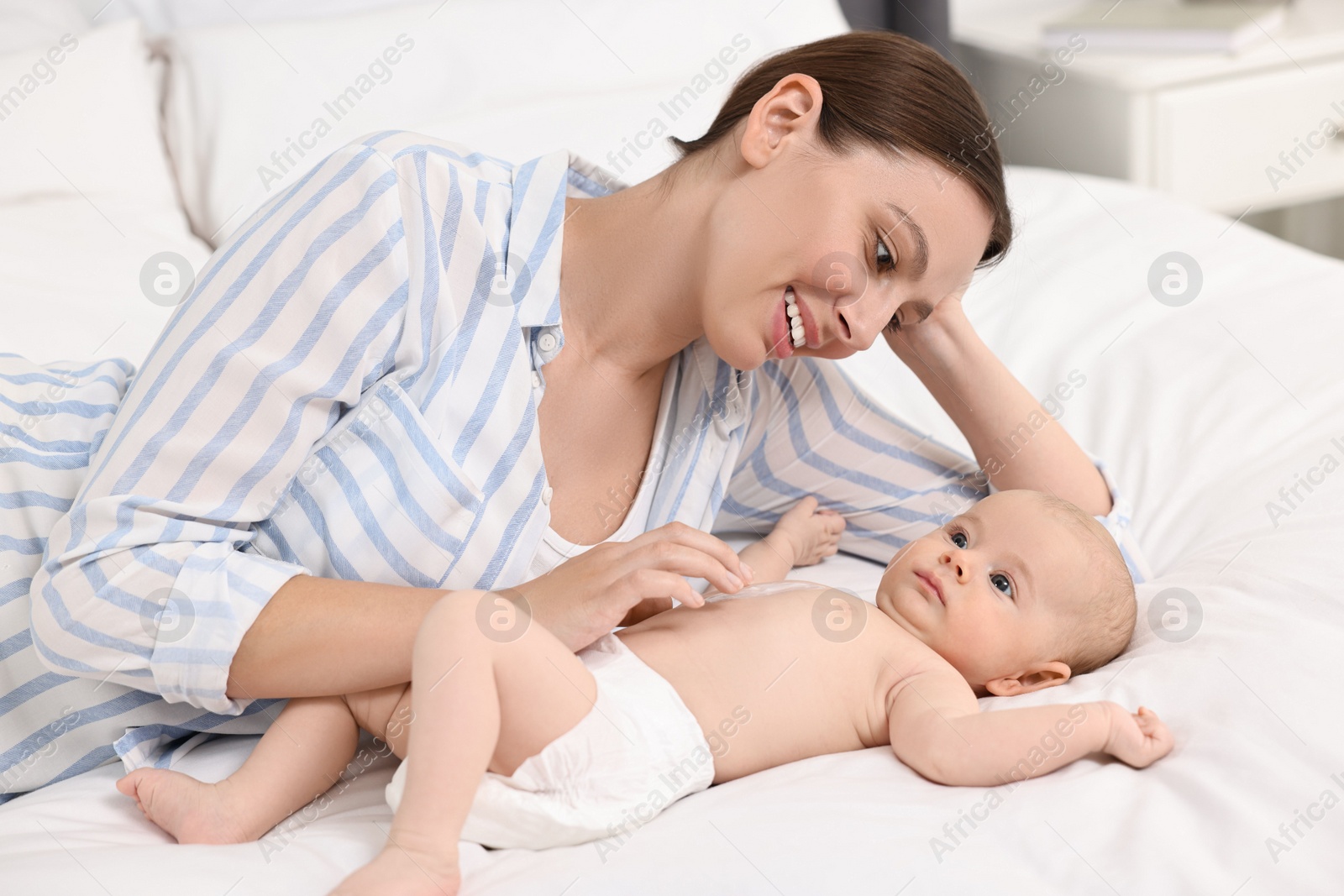 Photo of Happy young woman applying body cream onto baby`s skin on bed