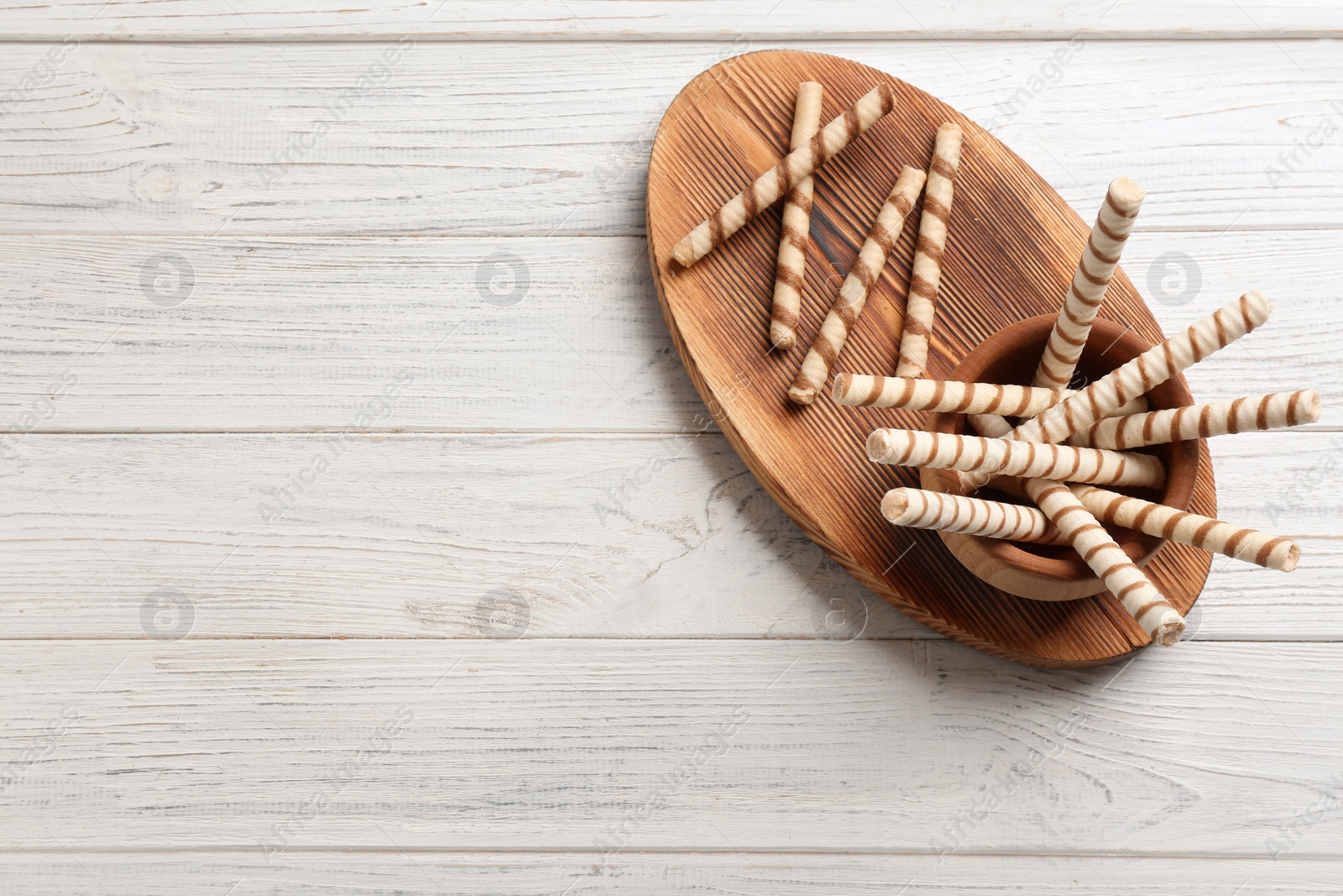 Photo of Bowl of delicious wafer rolls on wooden table, top view with space for text. Sweet food