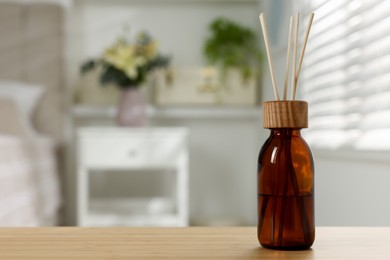 Photo of Aromatic reed air freshener on wooden table in bedroom. Space for text