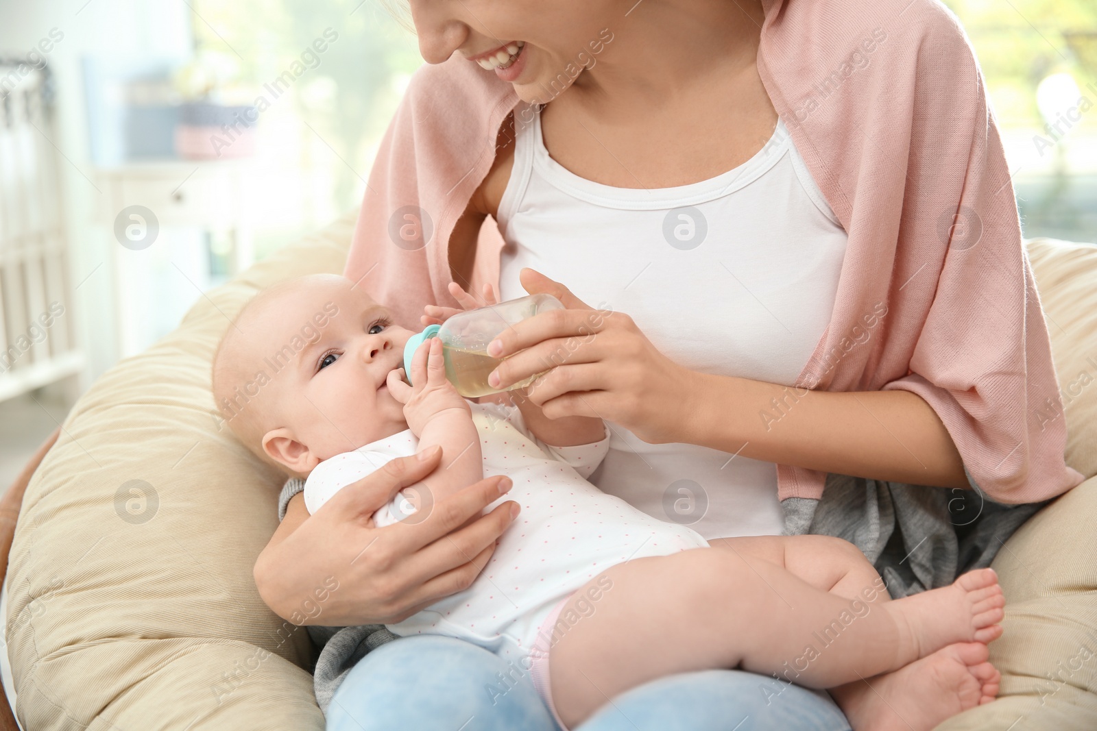 Photo of Lovely mother giving her baby drink from bottle in room, closeup