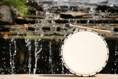 Drum with mallet near waterfall outdoors on sunny day, space for text. Percussion musical instrument