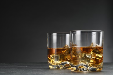 Photo of Whiskey and ice cubes in glasses on grey table, closeup. Space for text