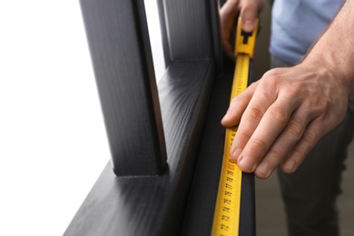 Photo of Man measuring wooden window frame indoors, closeup. Construction tool