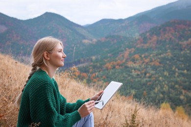 Photo of Young woman drawing on tablet in mountains, space for text