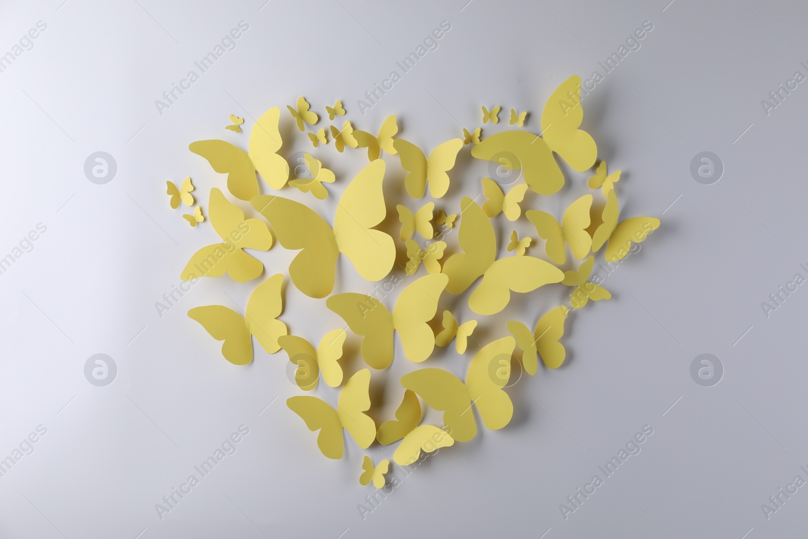 Photo of Heart shape made of yellow paper butterflies on light grey background, top view