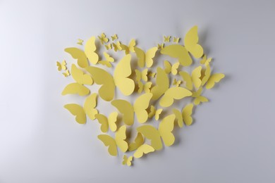 Photo of Heart shape made of yellow paper butterflies on light grey background, top view
