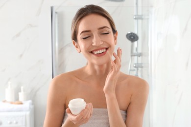 Photo of Young woman applying cream onto her face in bathroom