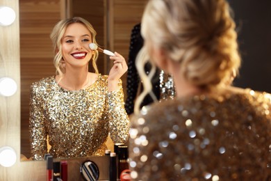 Beautiful makeup. Smiling woman applying powder with brush onto face in front of mirror in dressing room