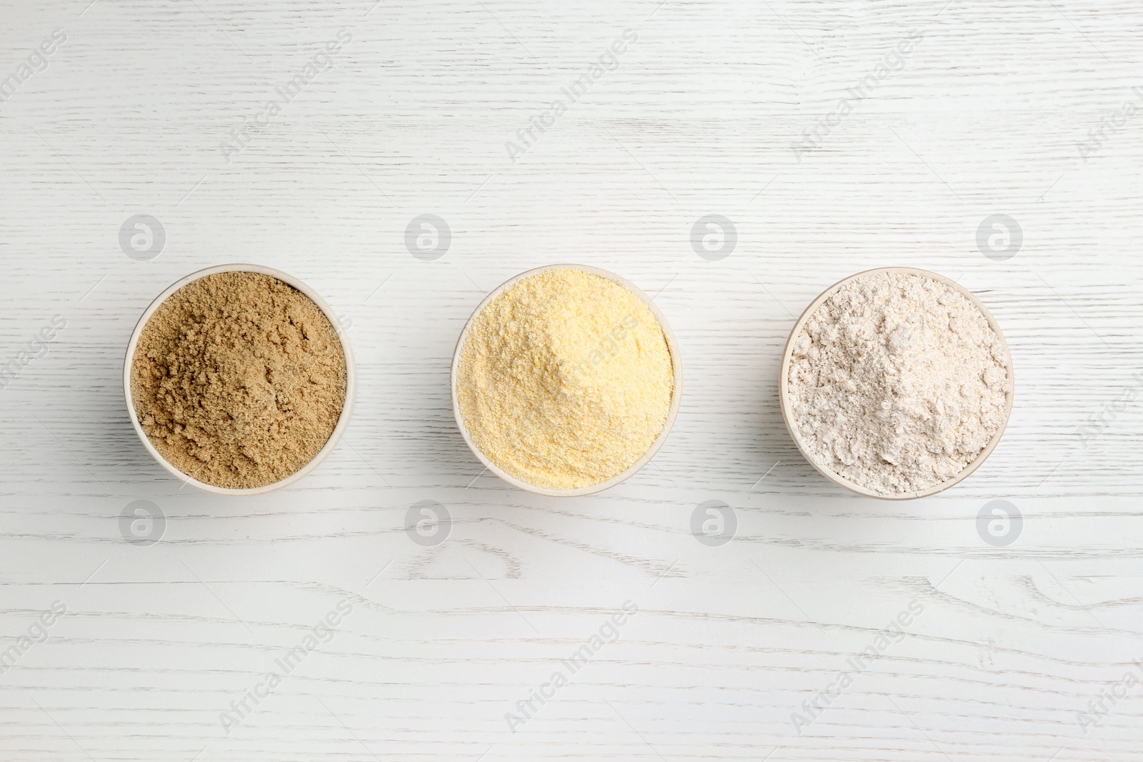 Photo of Bowls with different types of flour on white wooden background, top view