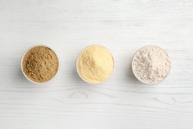 Bowls with different types of flour on white wooden background, top view