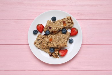 Photo of Tasty granola bars and berries on pink wooden table, top view
