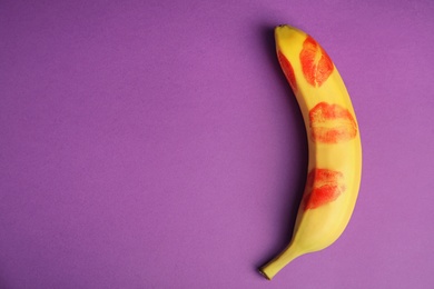 Top view of fresh banana with red lipstick marks on purple background, space for text. Oral sex concept